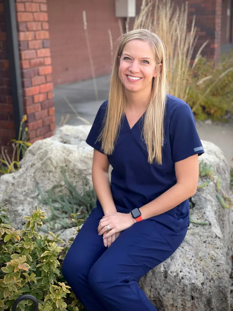 Dr. Alex Grieves in navy scrubs, sitting on a rock outside the clinic