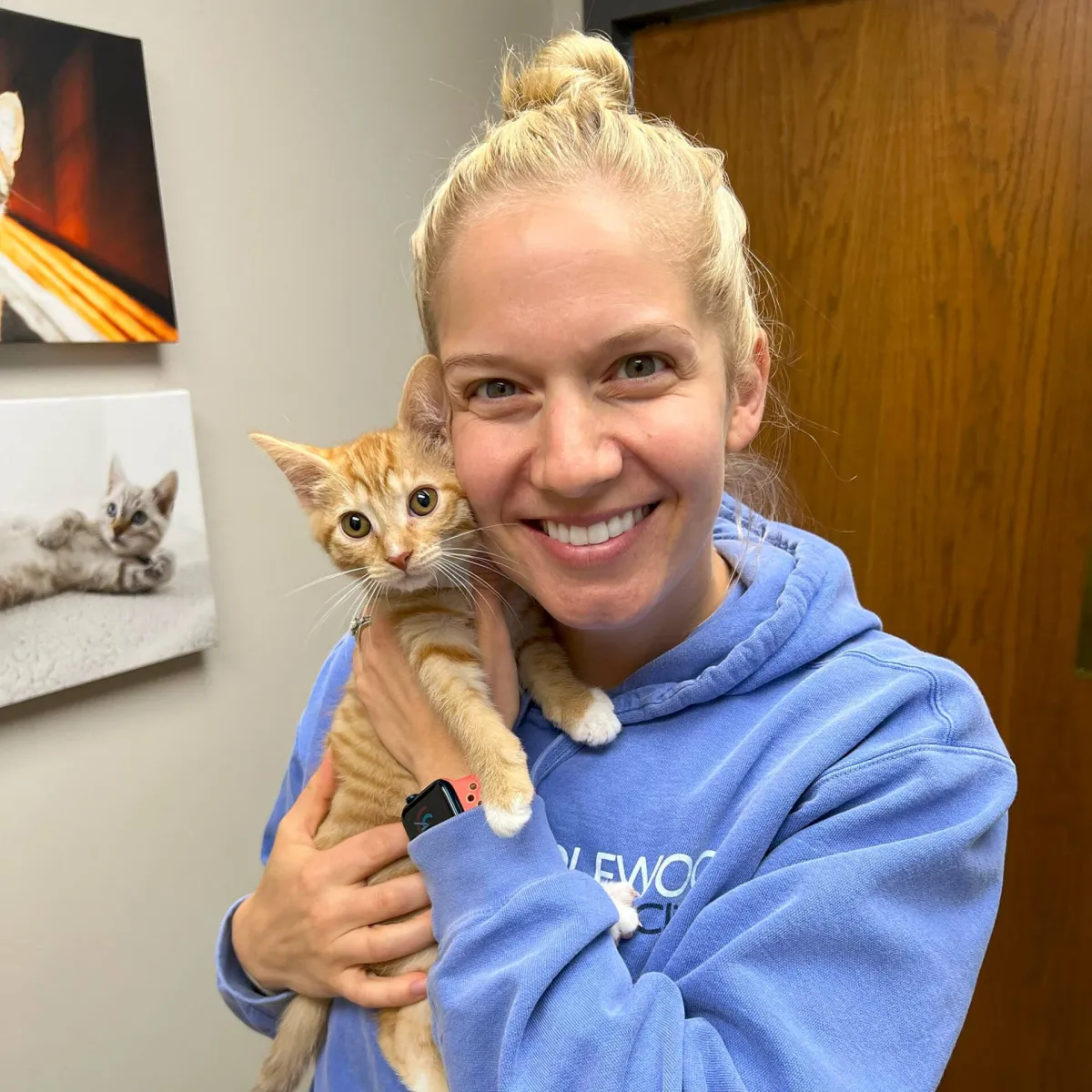 A smiling team member in a Candlewood hoodie cuddling an orange kitten